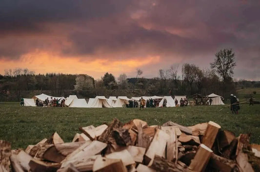 Campsite with tents and people at sunset, with a pile of wood in the foreground.
