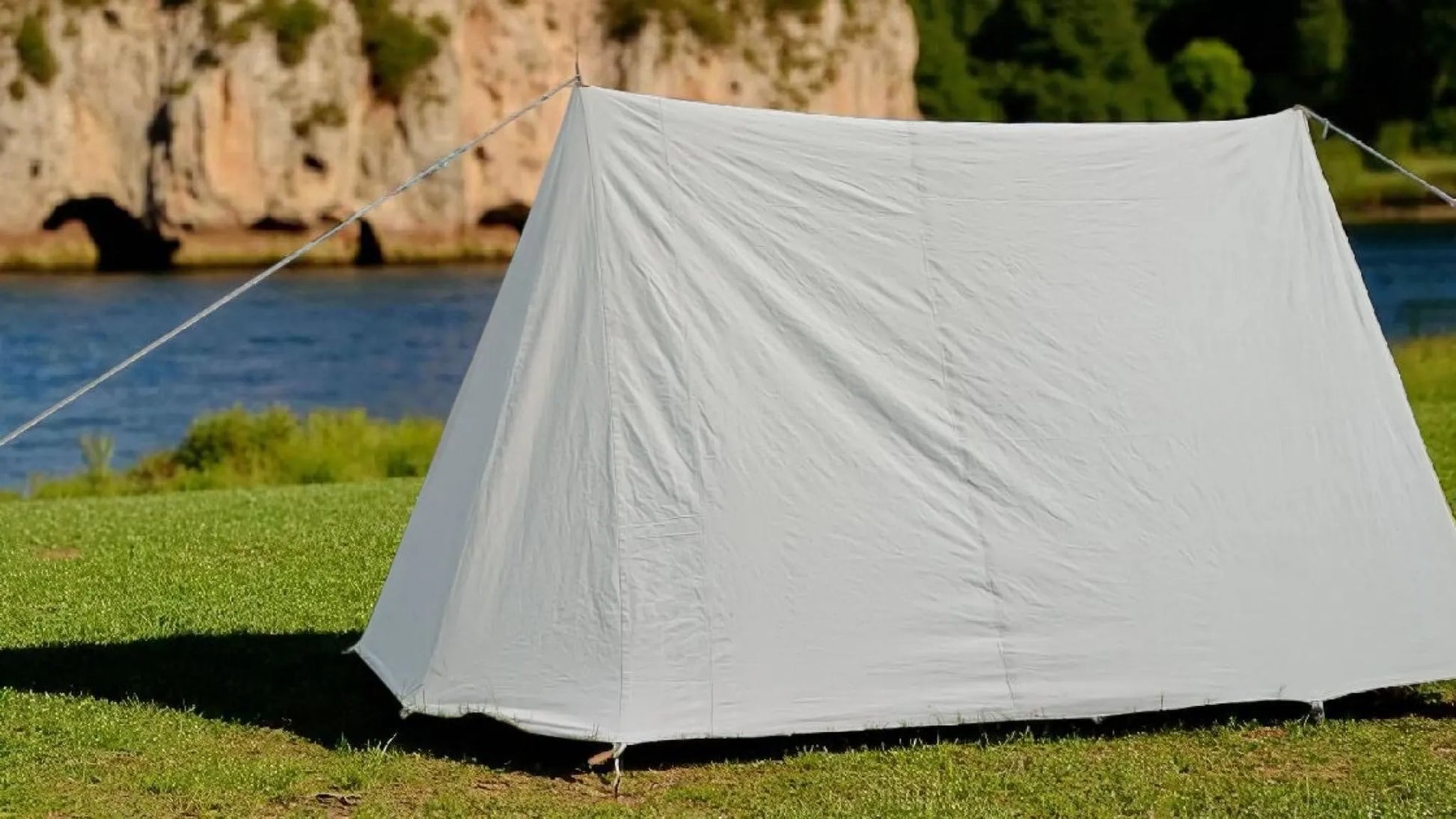 White tent set up on grass with a scenic background of water and cliffs.