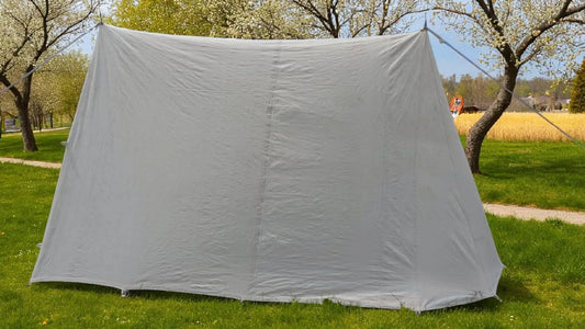 White tent set up on grass with trees and a clear sky in the background