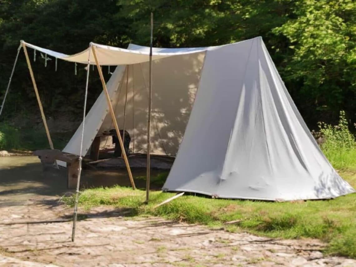 White canvas tent set up outdoors with greenery in the background