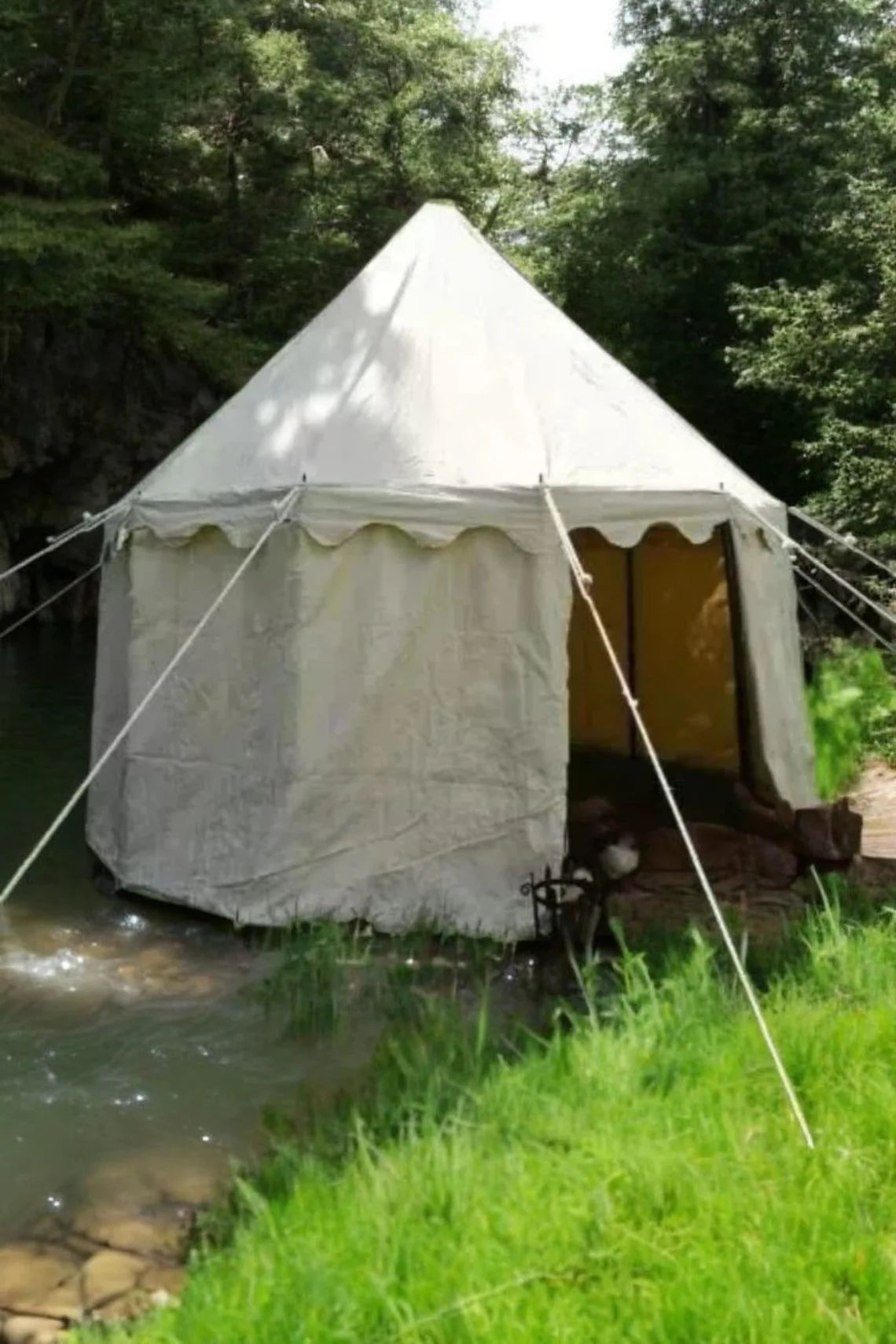 White bell tent with yellow interior in a natural setting by a stream