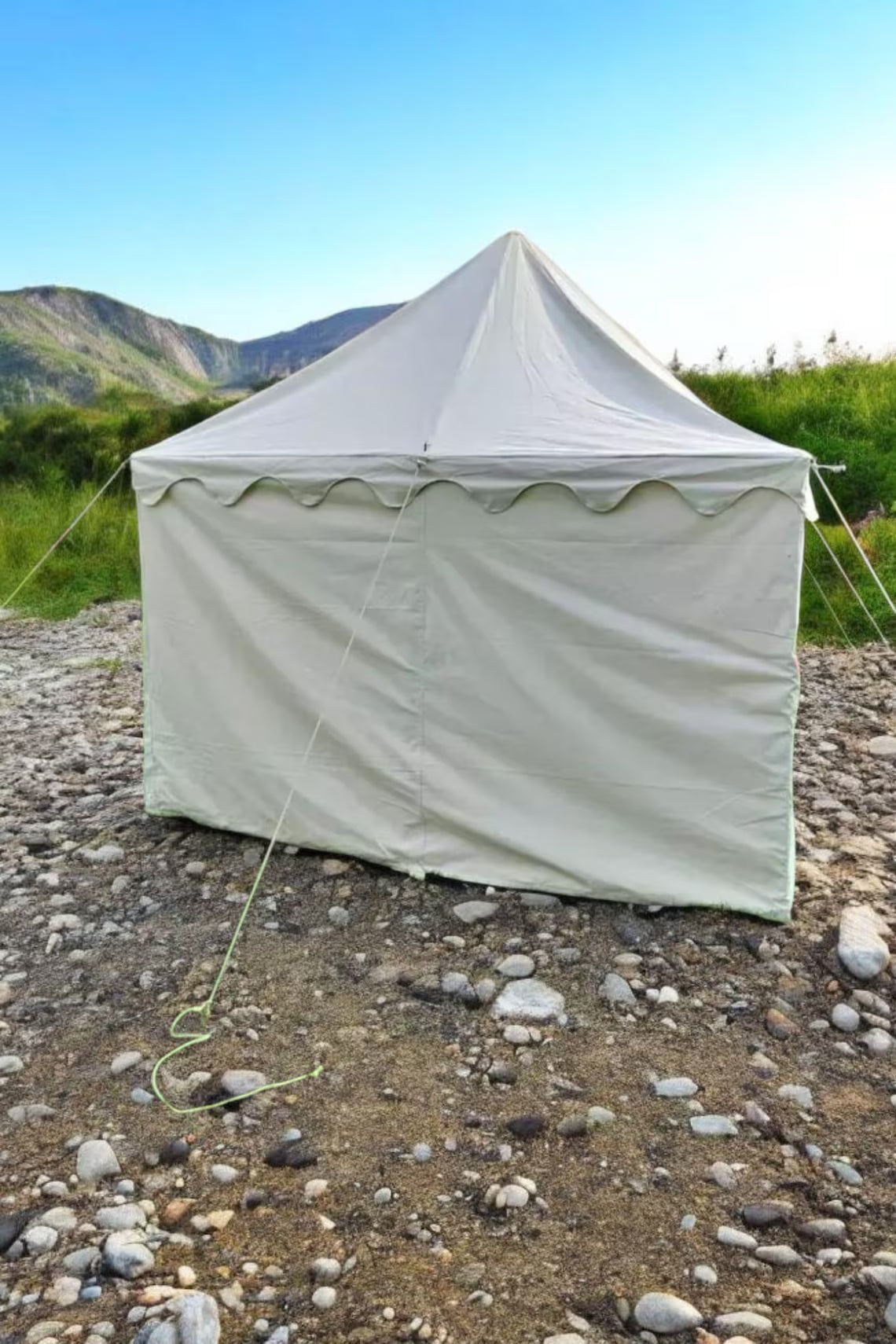 White tent set up on a rocky ground with mountains in the background