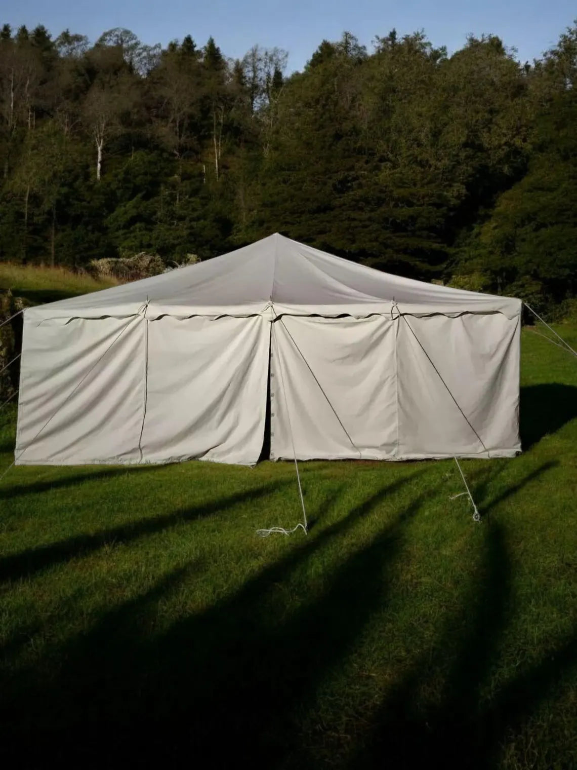 Beige tent with curtains on a grassy field with trees in the background