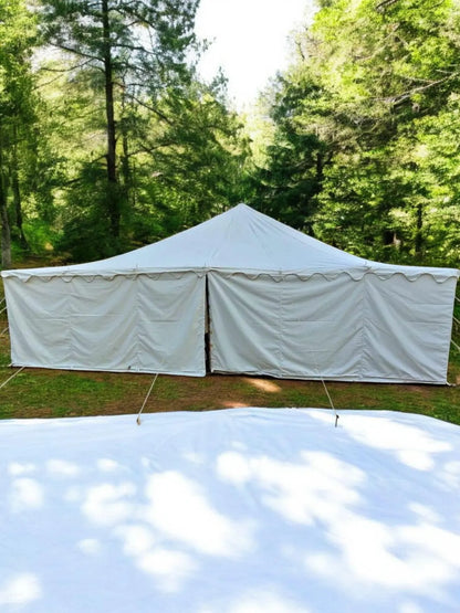 White tent with side walls set up outdoors in a forested area