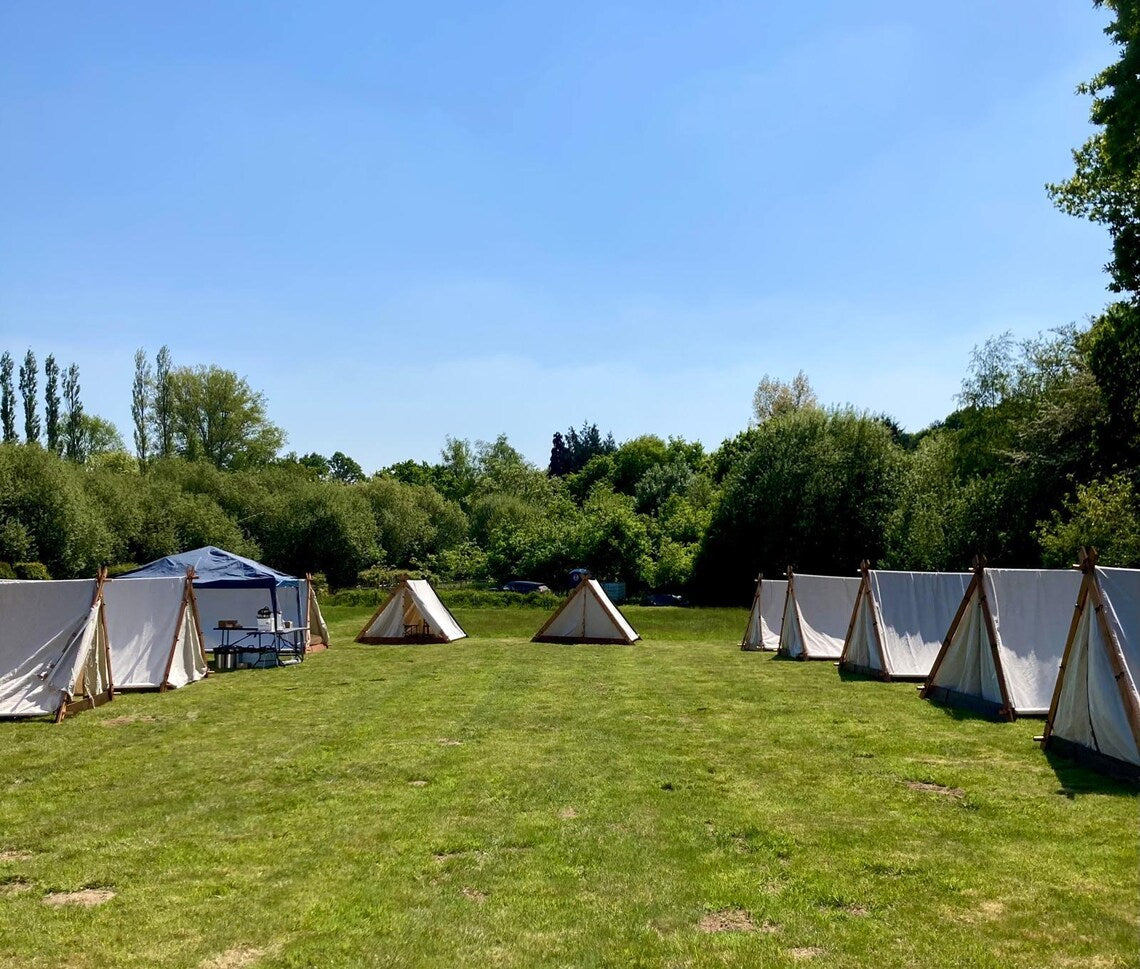 Row of tents set up on a grassy field with trees in the background