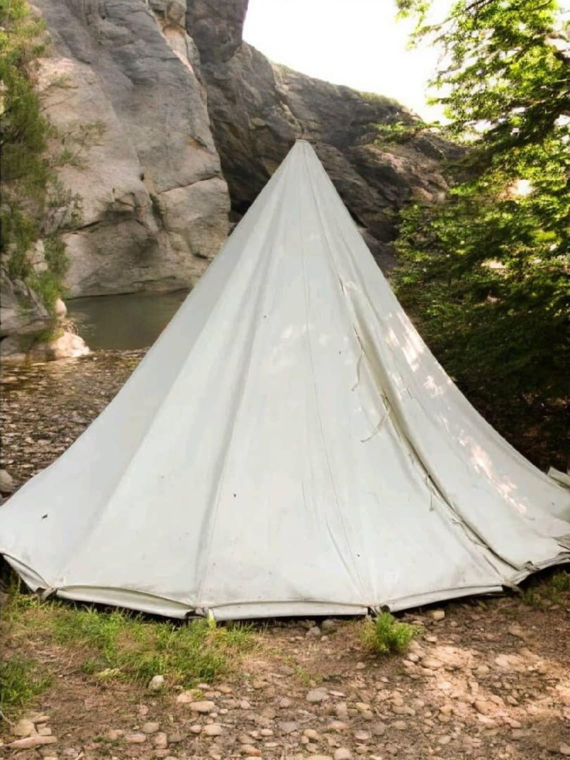 White tent set up in a natural outdoor setting with rocks and trees.