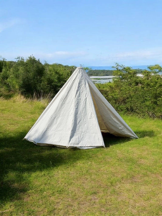 Tent set up in a grassy area with trees and a clear sky in the background