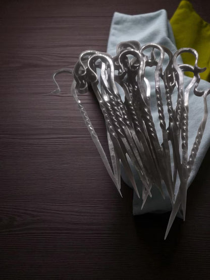 Set of metal skewers on a dark surface with a light blue napkin underneath.
