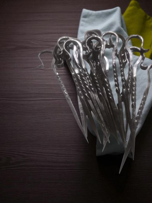 Set of metal skewers on a dark surface with a light blue napkin underneath.